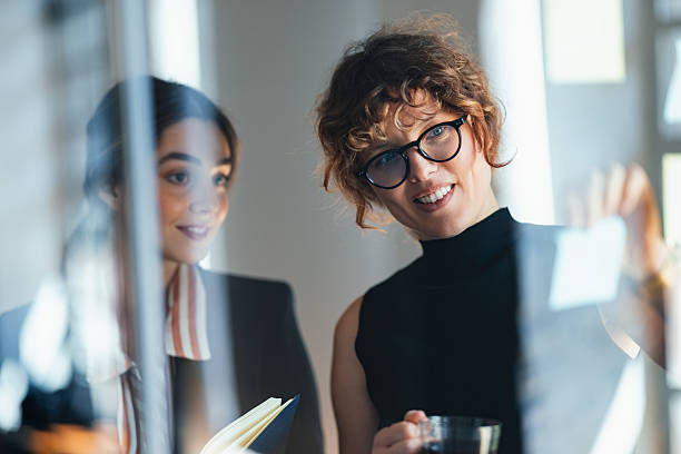 istock Professional Women Collaborating In Modern Office Reviewing Notes On Glass Wall 2244825289
