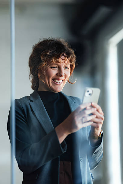 istock Professional Woman Smiling While Using Smartphone in Modern Office Corridor 2244825291