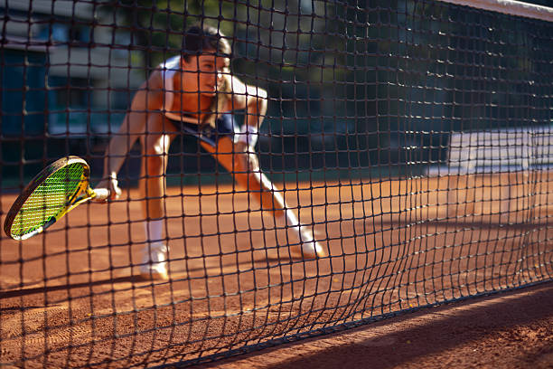 Close up of focused tennis net with blurred figure of man in background.