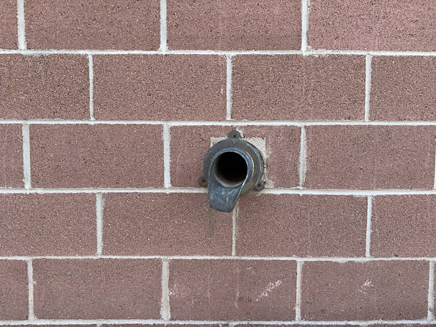 Metal spout extending from a brown cinder block wall, acting as a drainage pipe
