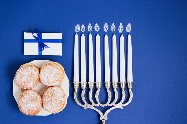 Celebration of Hanukkah. Candlestick with fried donuts, gift, on white and blue background