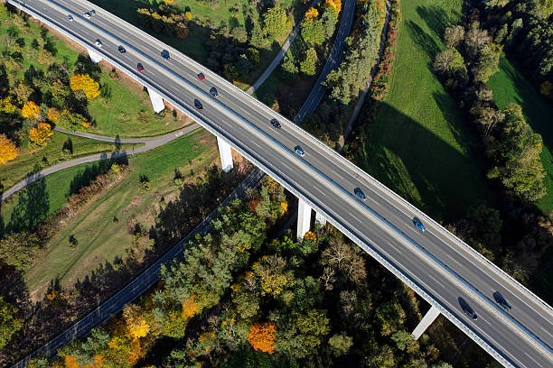 Aerial view of cars moving on a highway viaduct over a valley among green forests on a sunny day.