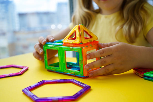 istock The photograph captures a little girl playing with magnetic construction blocks, assembling them into different designs on a yellow backdrop. 2244850472