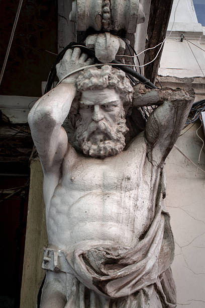 Antique stone atlas statue supporting a building balcony with electrical wires overhead.