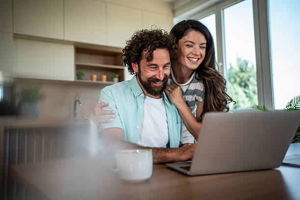 istock Happy couple laughing while browsing laptop at home kitchen 2244852410