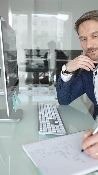 istock Businessman in a blue jacket thinking and brainstorming ideas while working on computer and taking notes in modern office. Business people concept 2244853664