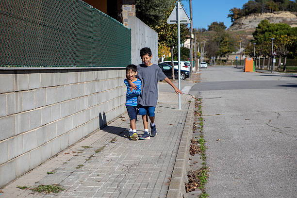 Two young brothers walking and hugging on a quiet residential street on a sunny day.