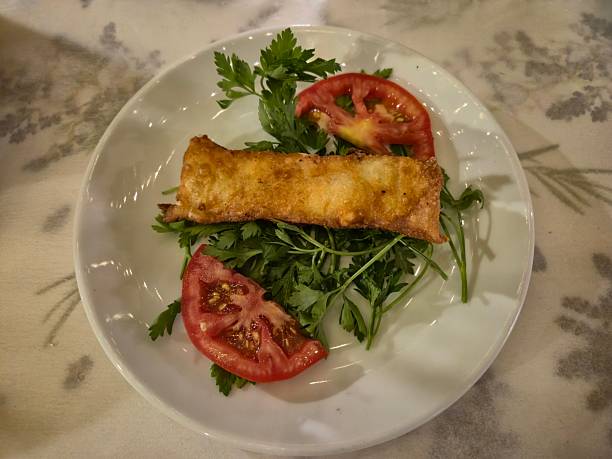 Fried filo pastry rolls with cheese filling, Turkish food -  Sigara Boregi -  Cigar Shaped Rolls. A single borek served with tomato and parsley