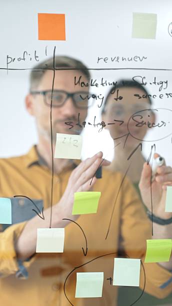 istock Business colleagues brainstorming, writing strategy notes on glass board, collaborating with colorful sticky notes in creative workplace meeting 2244865863