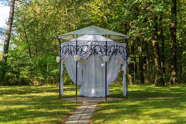 A lovely gazebo with white drapes stands in a peaceful forest, perfect for outdoor weddings or special gatherings in nature.