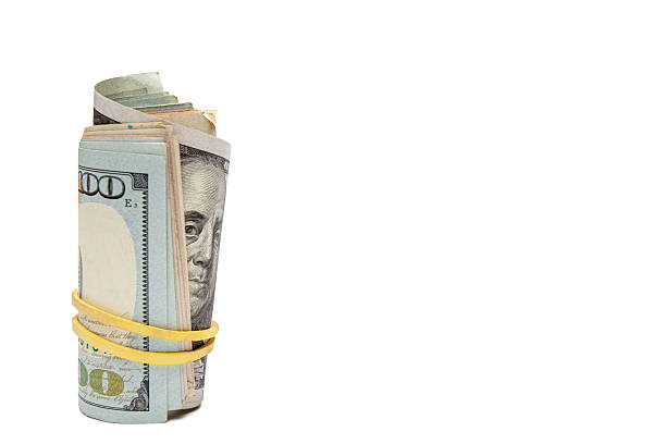 Vertical photo of a roll of US hundred dollar bills held by a rubber band, isolated on white background. Concept of finance, saving, payments, and business