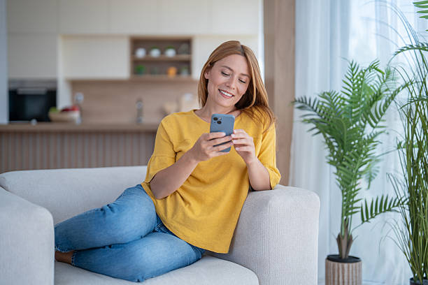 istock Smiling woman relaxing on sofa using smartphone at home 2244872843