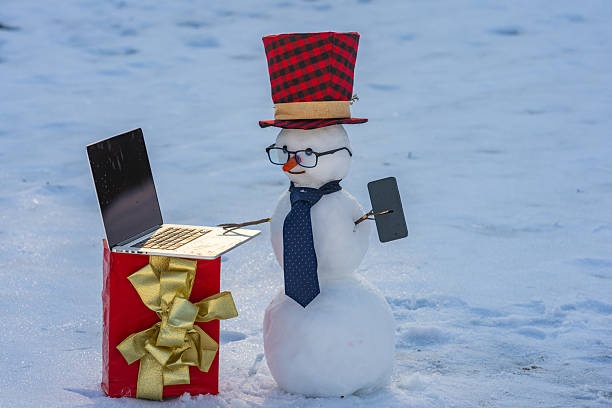 istock Snowman making a phone call and using laptop. Funny snowman talking on mobile in snow. Winter online greetings. Snowman businessman outside. Winter internet connection. Online snowman. 2244880434