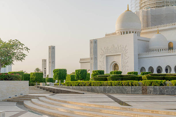 Sheikh Zayed Grand Mosque in Abu Dhabi, UAE, with ornate white domes, sculpted pillars, and geometric gardens on a warm, clear afternoon. Publicly available place, no tickets required.