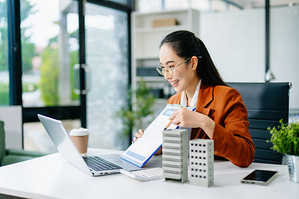 istock Mature real estate agent worker working with laptop and tablet at table in office and small house beside it. 2244884779