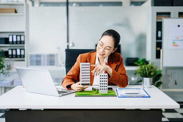 istock Mature real estate agent worker working with laptop and tablet at table in office and small house beside it. 2244884785
