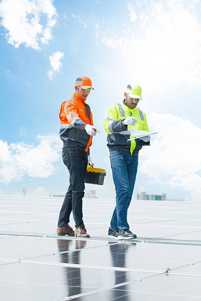 Two engineers inspecting and checking the operation and maintenance of solar cell panels installed on a building rooftop, representing renewable energy, green technology, and sustainable development.
