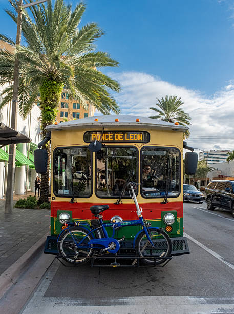 Miami Beach. USA. April.15.2025. Blue Miami Beach trolley driving along street with palm trees and buildings on background.
