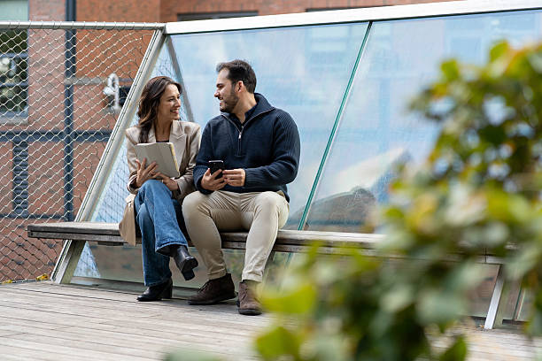 istock Two friends sitting and talking using technology outdoors 2244900094
