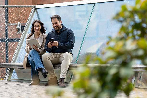 istock Two friends sitting and talking using technology outdoors 2244900097