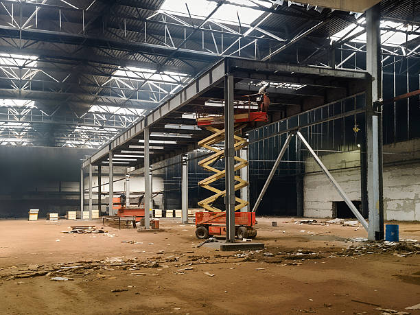 An industrial warehouse interior shows a scissor lift in use during construction or renovation work