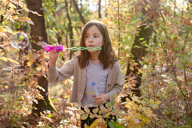 Young girl playing with soap bubbles in a vibrant autumn forest, embracing carefree childhood fun outdoors