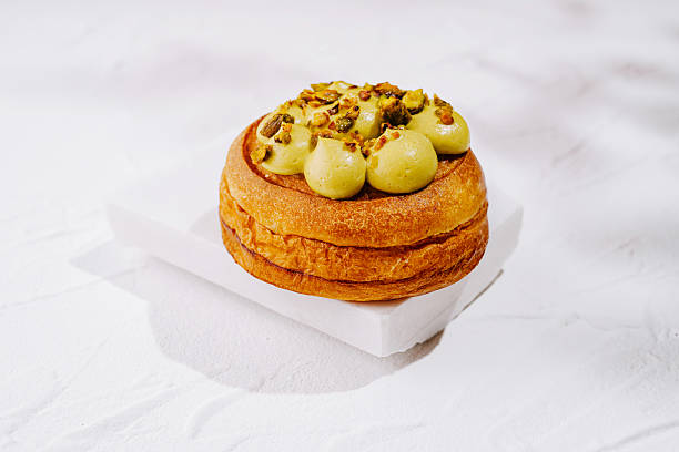 A richly baked pastry sits on a white plate, topped with smooth green mousse and crushed pistachios. The dessert looks inviting and fresh, perfect for a sweet treat any time of day.