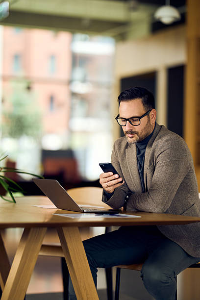 istock Professional Man Working On Smartphone At Modern Office Desk With Laptop And Documents 2244909791