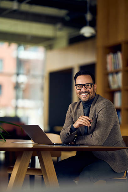 istock Professional Man in Blazer Smiling at Laptop in Modern Office Workspace Setting 2244909792