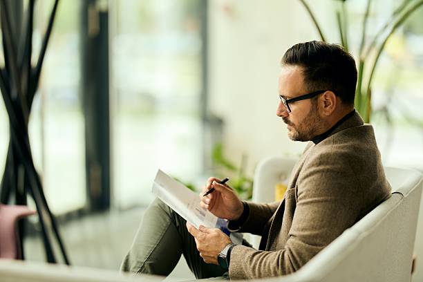 A professional man sits in a contemporary office lounge, reviewing a document with a pen.