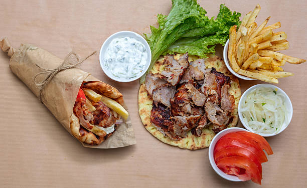 Greek gyros platter and wrap served featuring fries, tzatziki, lettuce, onions, and tomatoes upon the brown paper background under natural daylight, highlighting vibrant Mediterranean street food colors