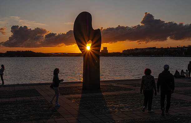 Stockholm, Sweden - 13 September 2025: Silhouette of people walking by a sculpture at sunset by the water.