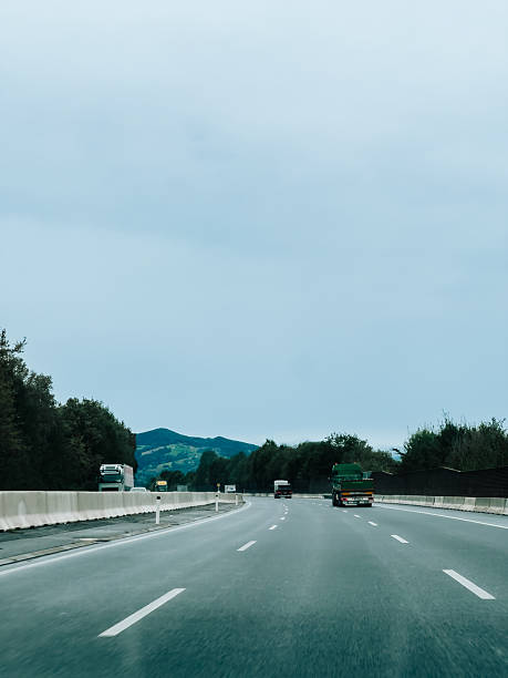 Trucks transporting goods driving on highway under cloudy sky, offering perspective of logistics and transportation in natural setting. Highway trucks hauling cargo, navigating asphalt lanes