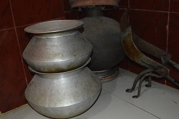 Weathered aluminum kettles stacked beside a traditional coal stove in a worn kitchen. The scene evokes nostalgia, warmth, and the charm of old kitchen tools and domestic life.