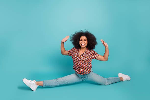 istock Young woman in a colorful shirt performs a full split against a bright blue background for lifestyle fitness and fashion advertising 2244919352