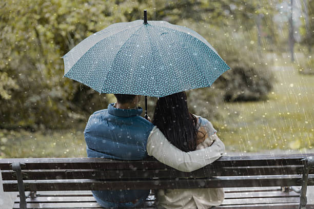 Happy young couple in yellow raincoats embracing in the nature during rainy day