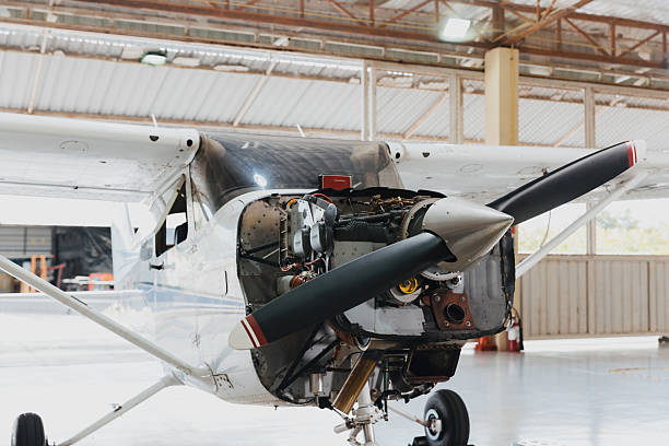 A Cessna aircraft sits in a bright hangar while mechanics work on its open engine compartment. Tools and equipment are nearby, indicating ongoing maintenance.