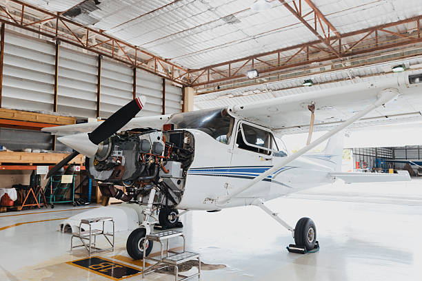 A small white airplane is stationed inside a hangar with its engine exposed. Maintenance work is being done, with tools and equipment around, highlighting the repair process.