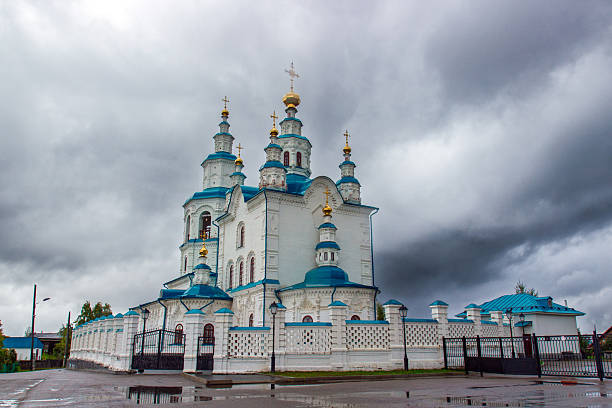 General view of Trinity Church under cloudy overcast sky in Yeniseysk, Russia. A white Orthodox church with blue domes and golden crosses. An architectural monument of the late 18th century