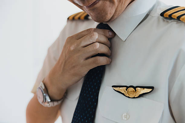 The pilot adjusts his tie and straightens his uniform, showcasing professionalism in preparation for an upcoming flight in a well-lit environment.