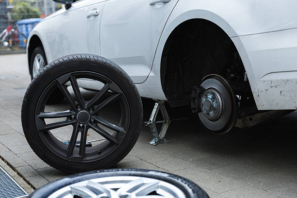 istock Car raised on jack during tire or brake replacement on paved surface. Power tools and jack stand visible, close-up of exposed brake rotor and suspension 2244935444