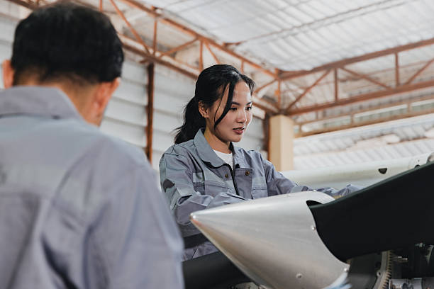 A skilled technician inspects and works on an aircraft engine in an aviation maintenance shop, collaborating with a colleague. The workspace is organized for safety and efficiency.