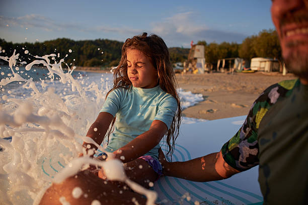Father and daughter having fun together playing with waves and surfboard on the beach