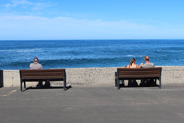 Jover, Tenerife, Spain, November 1, 2025: Three people admiring the scenery while sitting on two benches in Jover on the Atlantic Ocean, Tenerife, Spain