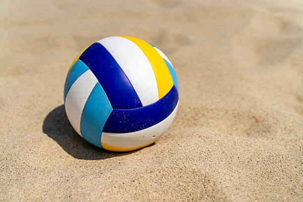 Volleyball resting on a sandy beach under bright sunlight. The ball's vibrant colors contrast with the sand, creating a lively summer scene.