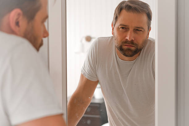 istock Confident handsome bearded man looking himself at the mirror. Pensive guy gazing thoughtfully. Captures introspection, grooming, hair care. Suitable for male health, lifestyle or personal care content 2244953432