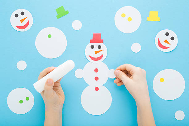 istock Little child boy hands creating and gluing snowman shape from white paper on light blue table background. Pastel color. Making winter elements. Closeup. Point of view shot. Top down view. 2244954825