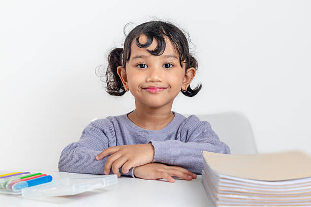 A smiling little Asian girl crossing her arms on her study table