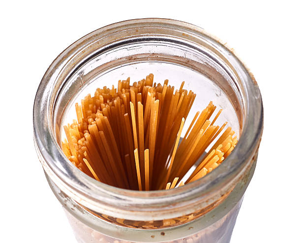 Glass jar filled with whole wheat spaghetti isolated on white, communicating pantry organization, dry storage, and wholesome ingredient readiness for cooking.