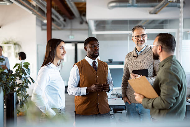 istock Multicultural Team of Three Men and One Woman Talking while Standing Together in a Contemporary Office 2244960267